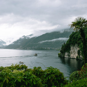 Lush green landscape with a lake and mountains under a cloudy sky