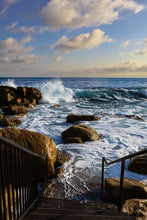 Stairs leading down to a rocky shoreline with waves crashing against the rocks.