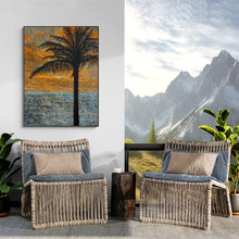 Two wicker chairs with cushions in a room with wall art of a palm tree and ocean, and another of mountains.